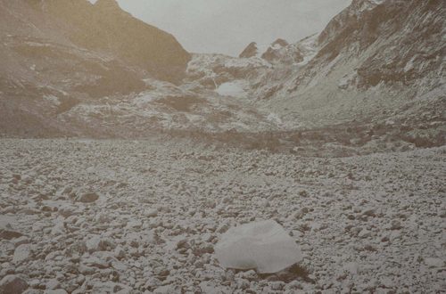 Greyscale image of a large rock in an expanse of stones with hills behind.