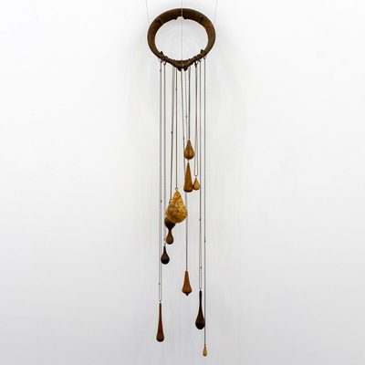 Wooden teardrop-shaped pendants hang on metal chains from a large ring, which has been mounted on a white wall.