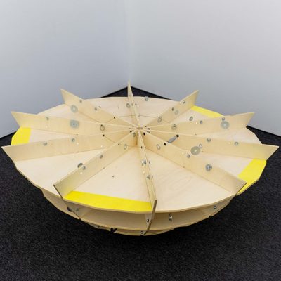A large plywood sculpture in the shape of a spinning top. The top is divided into radial sections with wires criss-crossing between. Washers are suspended on the wires, which clank together as the sculpture is moved.