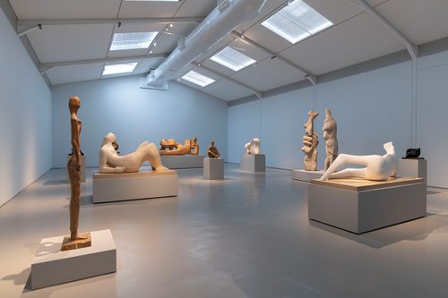 Wide shot of a large gallery space, filled with large figurative sculptures by Henry Moore, carved from wood and stone.