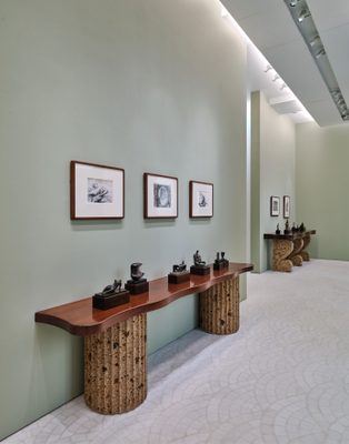 Interior photo of the Gagosian Paris art gallery. Two wooden tables by Malaparte display fourteen small bronze sculptures by artist Henry Moore. Above the tables are five framed drawings, also by Moore.