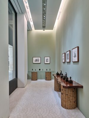 Interior photo of the Gagosian Paris art gallery. Two tables by Malaparte, one glass and one wood, display twelve small bronze sculptures by artist Henry Moore. Above the tables are five framed drawings, also by Moore.
