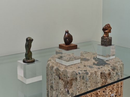 Three small bronze sculptures by artist Henry Moore, displayed on a glass table.