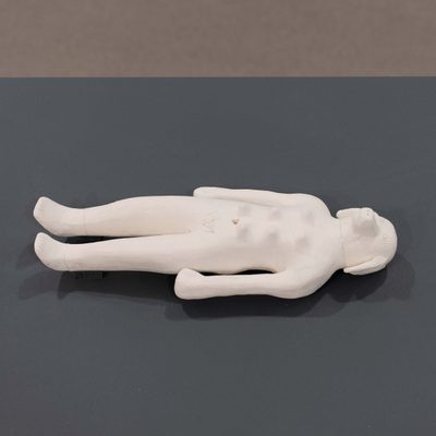 A white sculpture with both dog and human features lying on its back.