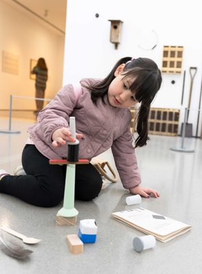 A young girl playing with an Explorer Bag in a gallery, balancing blocks to make a sculpture.
