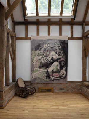 A tapestry in shades of pink and green, depicting one of Henry Moore's WW2 Shelter Drawings.. There is a vintage cane rocking chair just in front of the bottom left corner.