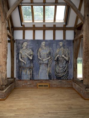 A blue toned tapestry depicting three women, hanging in a wood-beamed barn with skylight above.