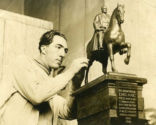 Sepia photo of a man putting the finishing touches to a model for a public sculpture of a military man riding a horse.
