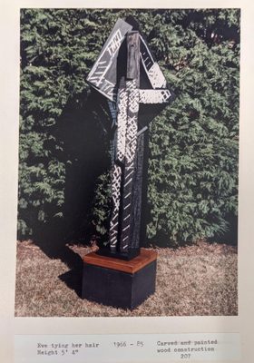 Abstract sculpture by Anthony Hatwell, constructed from wood and painted black with white lines. It gives the impression of a standing figure with arms raised behind their 'head'.