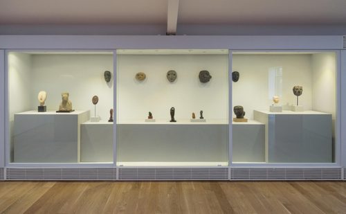 A display case set into the wall holding small sculptures of heads and masks.