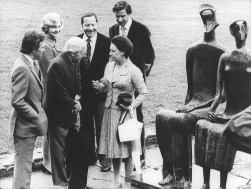 A black and white photo showing Henry Moore talking with Princess Margaret. They are standing next to Moore's famous sculpture 'King and Queen'