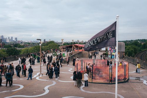 Hundreds of people attending an outdoor display of sculpture on a concrete rooftop space.