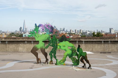A colourful metal sculptures of human-plant hybrid characters, displayed on a concrete rooftop space with the London skyline behind.