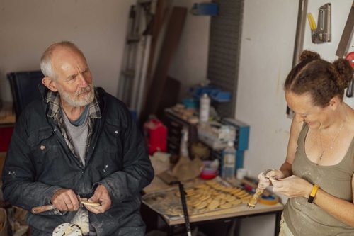 A man and a woman using hand tools to carve digestive biscuits from plaster. Behind them is a large pile of finished plaster biscuits and a large desk vice.