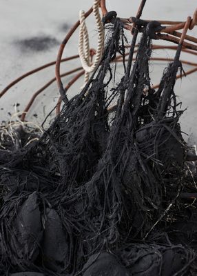 Close up view of tangled, matted fibres and fabric, painted or dyed black, attached to a rusted metal frame.