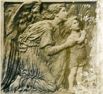 Relief sculpture of an angel, who is kneeling down in a motherly fashion by a small child holding a sheaf of wheat.