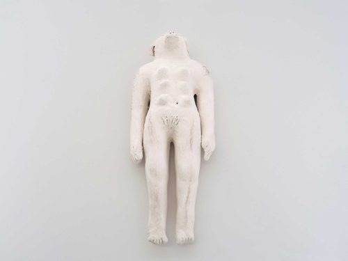 A white sculpture with both dog and human features lying on its back.