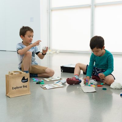 Two children in a gallery playing with explorer bags.