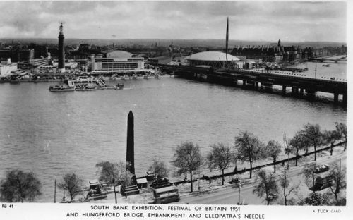 Black and white photo of a wide river with a bridge. Across the river is a dock with a few boats moored, and the exhibition spaces used for the Festival of Britain.
