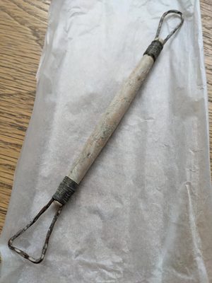 A wooden modelling tool, with loops of metal at both ends.