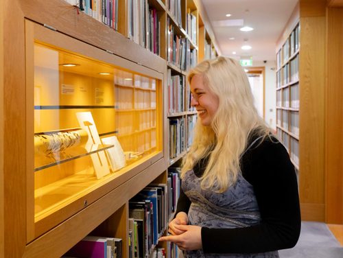 A woman with blonde hair is looking into a display cabinet, smiling.