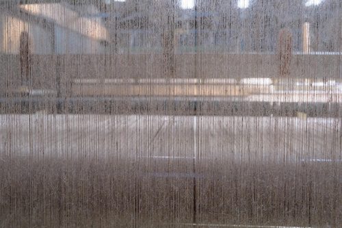 Close-up photo of strands of yarn passing through a loom.