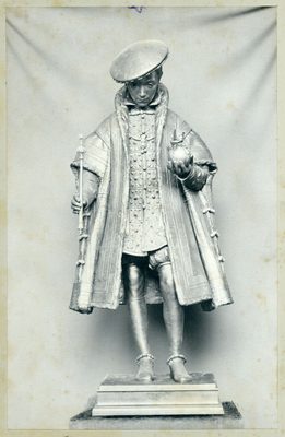 Black and white photo of a full-figure sculpture of a boy in upper-class Tudor-era clothing, possibly a prince, who is holding a small sceptre and a decorative orb.