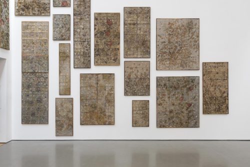 Around a dozen 'taxonomy boxes' of varying sizes, mounted to a white gallery wall. The wooden boxes are divided into compartments, some containing cocoons, and covered over with a semi-transparent mesh screen.