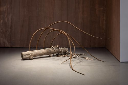 Sculpture made from a driftwood log, with four long, rusted metal spikes extending up and out from it in long, fluid curves resembling a breaking wave.