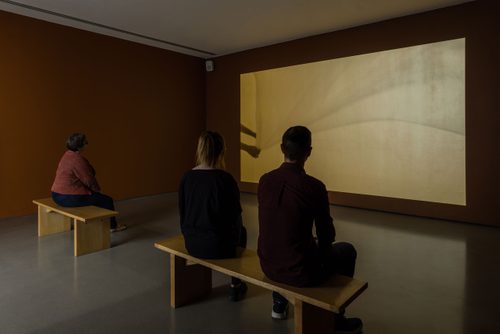 Three people sit watching Lungiswa Gqunta's film 'Gathering', which is being projected onto the gallery's walls.