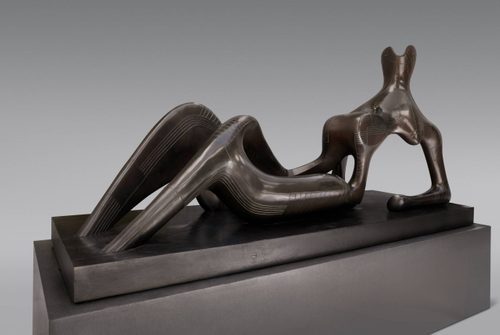 A studio photo of a bronze reclining figure sculpture, with a dark patina and incised line details. The work is resting on a dark grey plint.