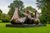 A large abstract bronze sculpture by Henry Moore. It is made of three parts locking together, somewhat resembling vertebrae. It is displayed on a low plinth in a field with trees behind.