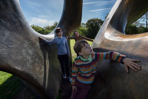 A family of three standing between the rings of Henry Moore's sculpture Double Oval.