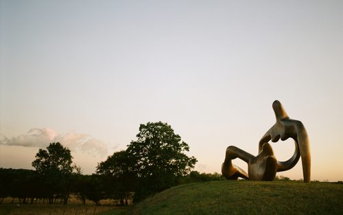 A photo of Henry Moore's huge bronze sculpture 'Large Reclining Figure' with the sun setting behind it