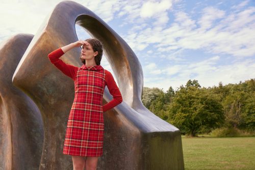 A model, wearing a red checked dress, stand looking into the distance in front of Henry Moore's sculpture 'Double Oval'.