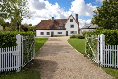 White, open gates lead along a path to Hoglands, a white painted former farmhouse with a red tiled roof.