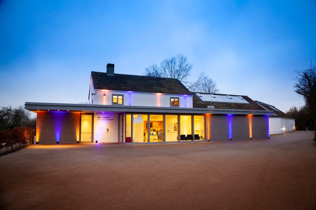 A white building with contemporary style entrance canopy. It is lit up in pastel colours for an evening party.