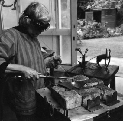 An older woman wearing safety goggles welding together two pieces of metal.