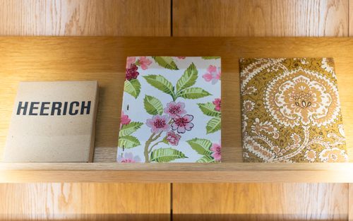 Shelf displaying three books; one is plain brown with the title 'Heerich', while the other two have floral patterns on their covers but no text.