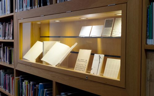 Display cabinet full of artists' books, set into library shelving.