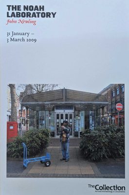 A blue exhibition flyer, with a photo of a man holding a large rabbit in front of a tourist information building. Text on the flyer reads 
