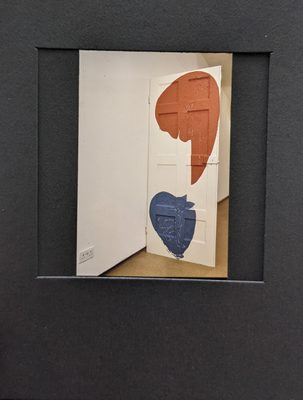 Art installation featuring a white door painted with a large red comma shape at the top and a smaller, rounder blue shape beneath.