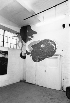 Interior of a brick building, possibly a former warehouse. Painted across two of the white walls and part of the ceiling is a mural of faces, human figures and a wolf.