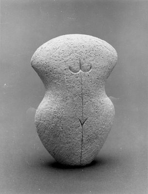 A small curved stone has had some simple lines carved into it to appear like a female body.