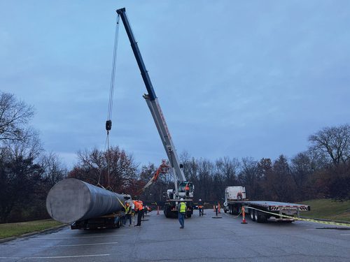 A crane lifting a large metal cylinder onto a long flatbed lorry. A sizeable portion of the cylinder overhangs the end of the lorry.