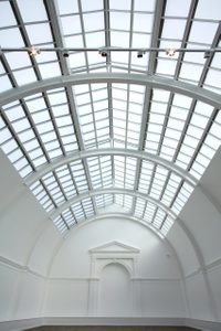 View looking up at the arched, glass ceiling of a white gallery space.