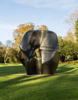 A large abstract bronze sculpture in a field. It is made of two interlocking pieces stacked on top of each other, with a hole in the middle.