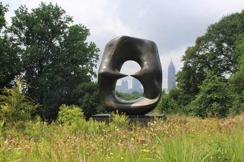 A large oval sculpture, made of bronze, sited in a flowering meadow with the Atlanta skyline visible in the background.