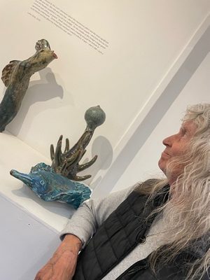 A woman with grey hair looking at small ceramic sculptures of various fantastical creatures.