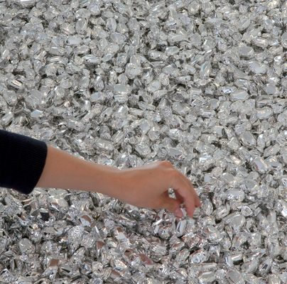 A hand is reaching out to a pile of sweets wrapped in silver foil, which cover the floor.